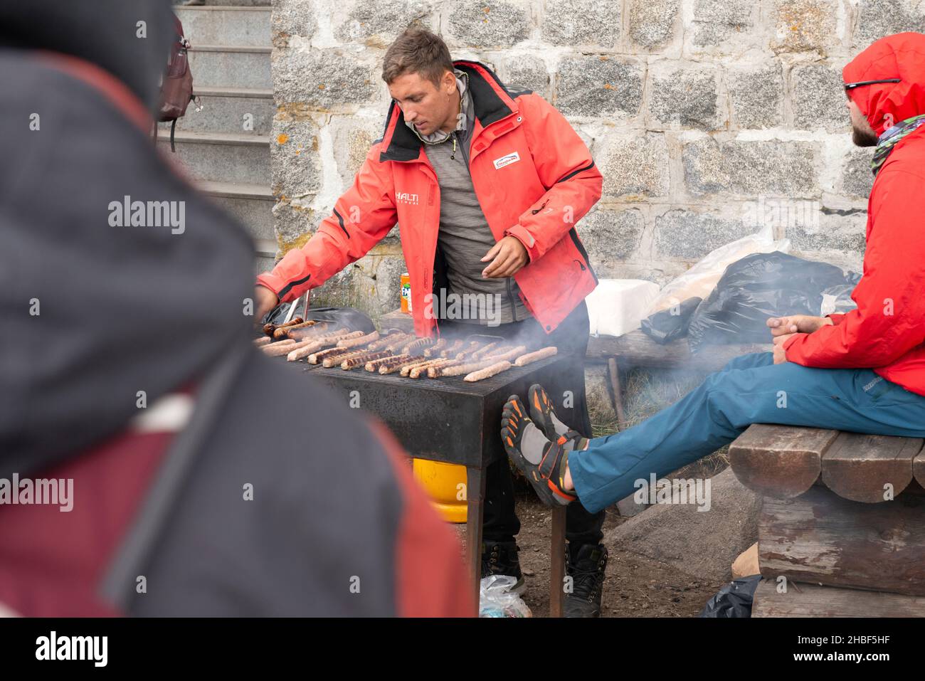 Mann an einem Grill, der Essen im Freien vor der Black Peak Hütte um 2290m Uhr im Vitosha Berg, Sofia, Bulgarien, zubereitet Stockfoto