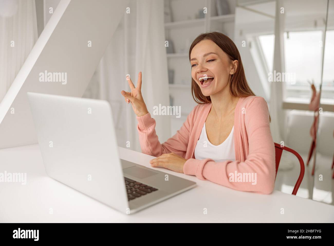 Lächelnde, hübsche Dame, die während eines Videoanrufs einen Laptop benutzt Stockfoto