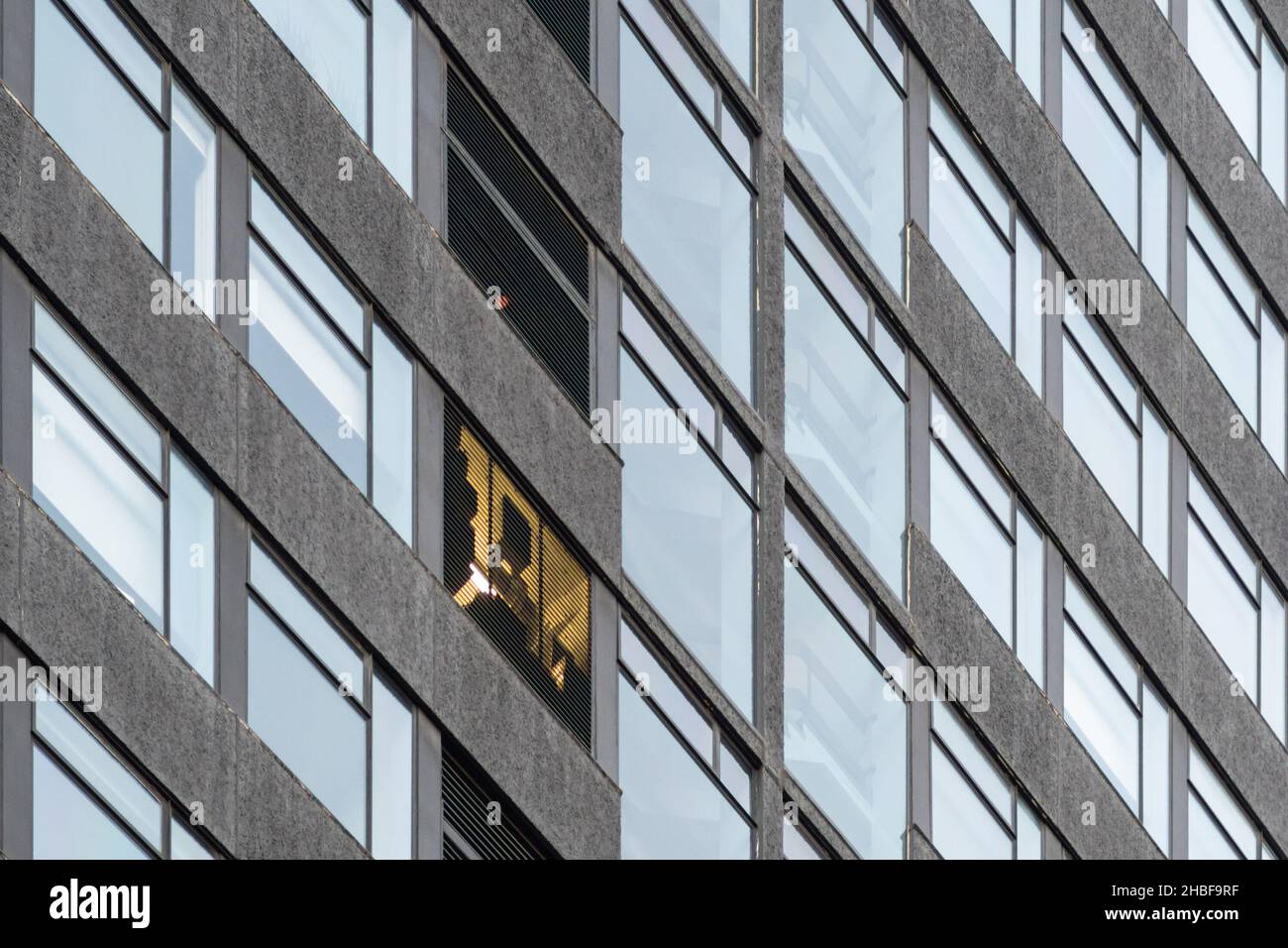 Fenster einer Hochhausfassade. Sichtbar ist eine Lampe in einem scheinbar wie ein Wartungsschacht oder ein Aufzug/Aufzug-Motorraum. Architektur, Großbritannien Stockfoto