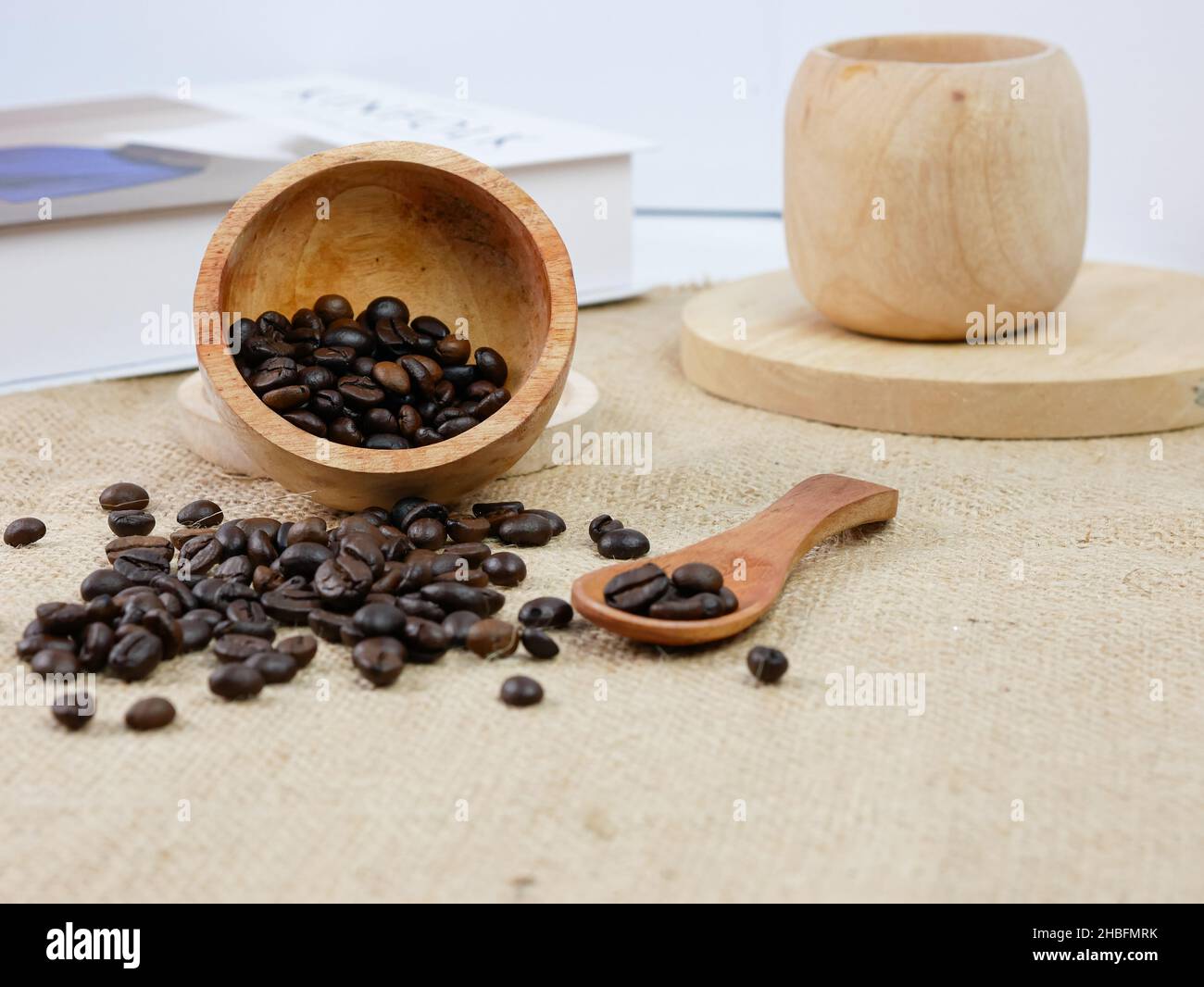 Hölzerne Tasse Kaffee mit Kaffeebohnen und Buch mit verschwommenem Hintergrund. Morgendliche Aktivitäten Stockfoto