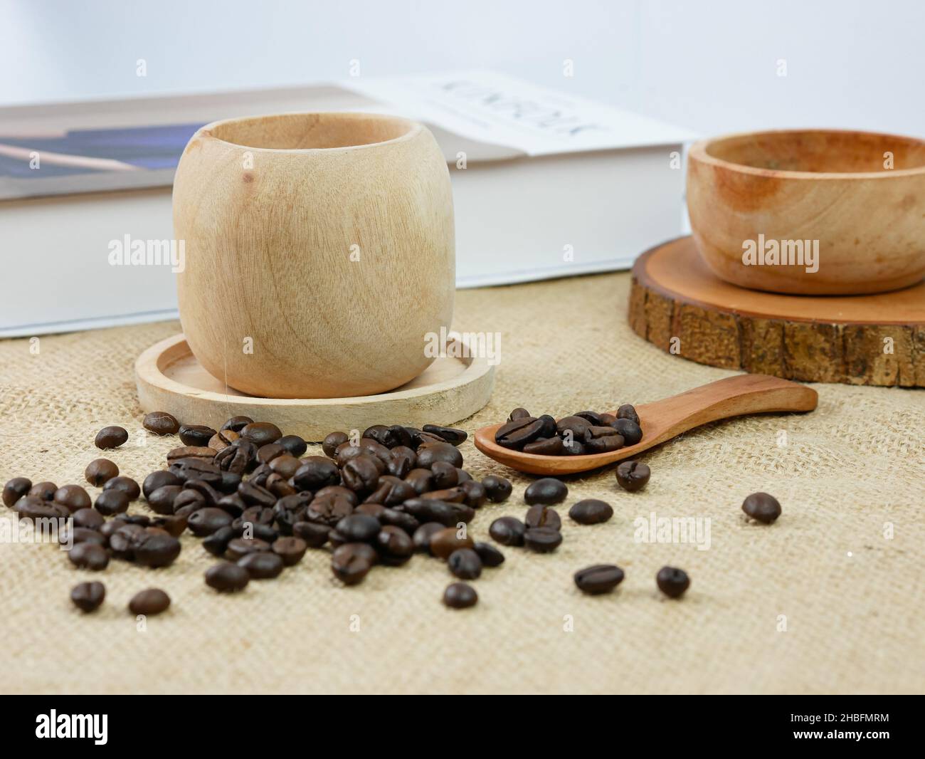 Hölzerne Tasse Kaffee mit Kaffeebohnen und Buch mit verschwommenem Hintergrund. Morgendliche Aktivitäten Stockfoto