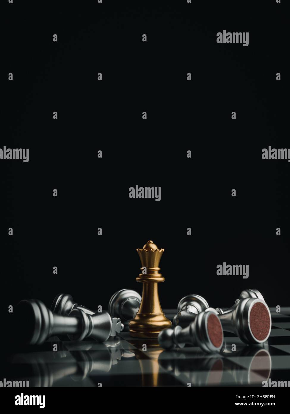 Das Schachstück der goldenen Königin steht mit fallenden silbernen Schachfiguren auf einem Schachbrett auf dunklem Hintergrund mit Kopierraum, vertikalem Stil. Führung Stockfoto