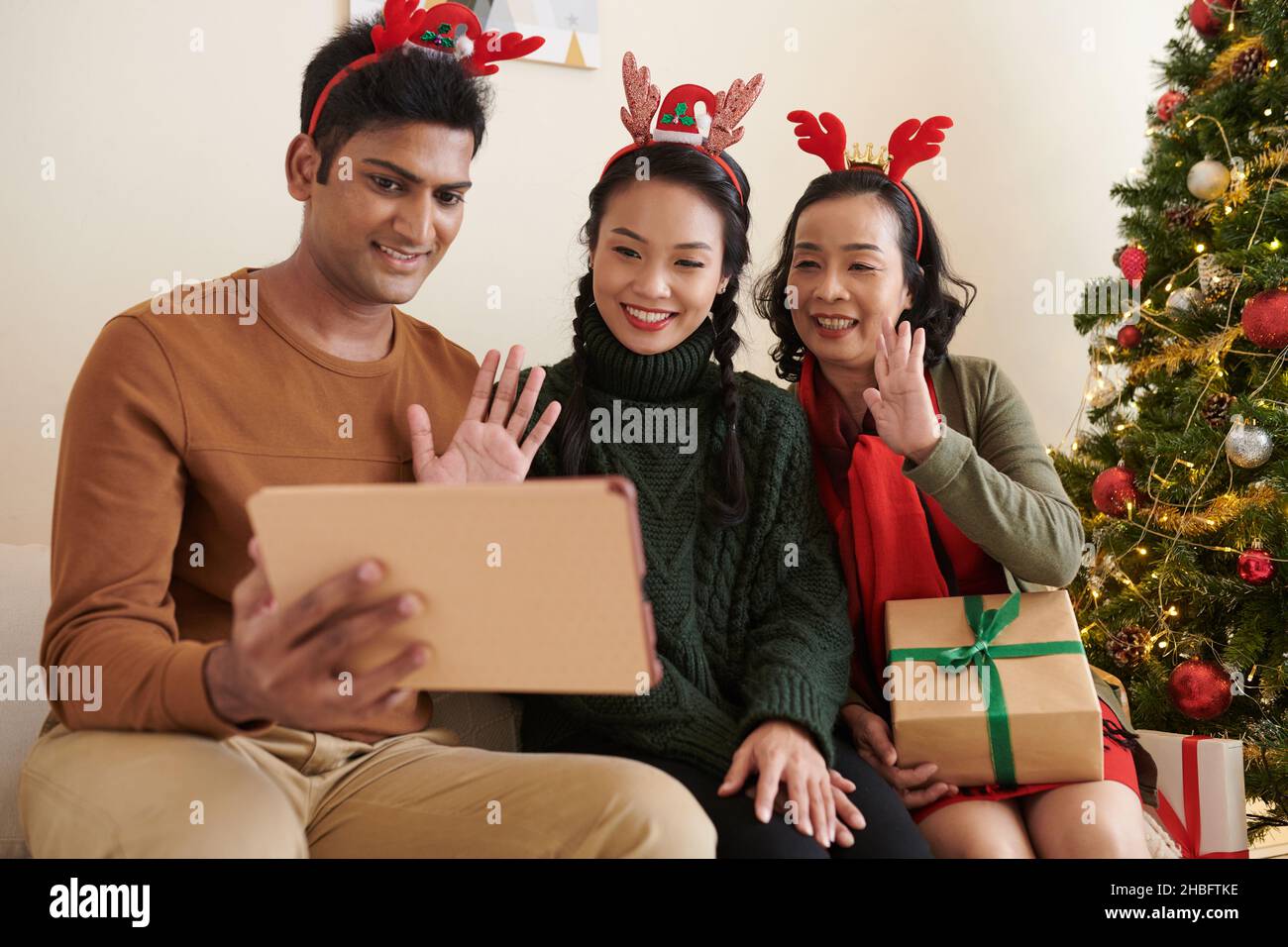 Lächelnde Familienmitglieder winken mit den Händen, als sie Verwandte aus einer anderen Stadt per Video anriefen, um frohe Weihnachten zu wünschen Stockfoto