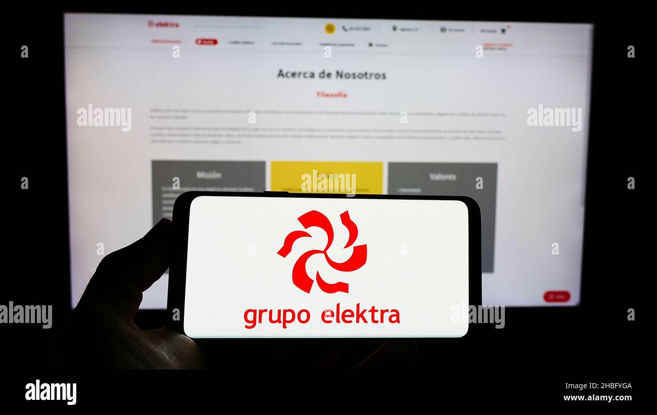 Person, die das Smartphone mit dem Logo des mexikanischen Einzelhandelsunternehmens Grupo Elektra auf dem Bildschirm vor der Website hält. Konzentrieren Sie sich auf die Telefonanzeige. Stockfoto