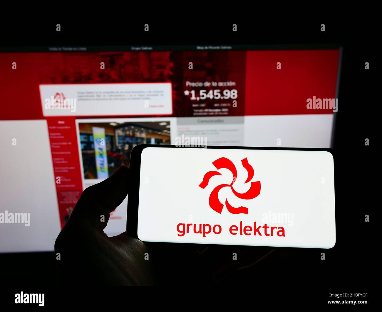 Person, die ein Mobiltelefon mit dem Logo des mexikanischen Einzelhandelsunternehmens Grupo Elektra auf dem Bildschirm vor der Unternehmenswebseite hält. Konzentrieren Sie sich auf die Telefonanzeige. Stockfoto