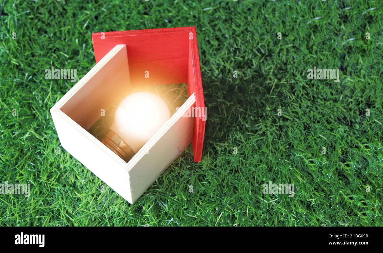Konzept für grüne Energie, Öko-Haus und erneuerbare Energien. Miniaturhaus und Glühbirne auf grünem Gras. Stockfoto