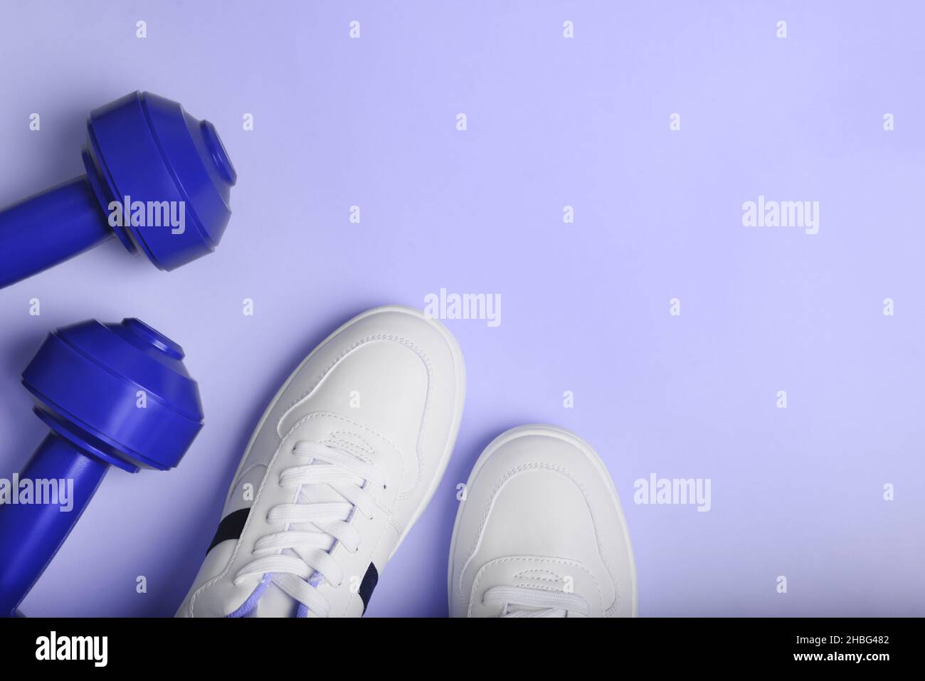 Weiße Sport-Sneakers Schuhe und blaue Kurzhanteln auf dem blauen Hintergrund. Stockfoto