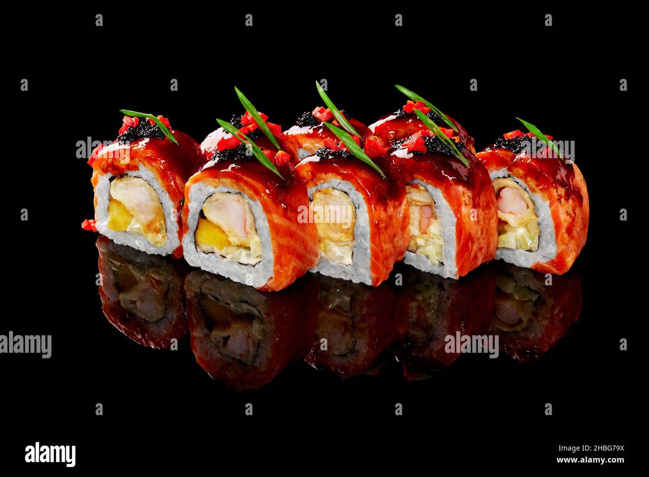 Gebratene Lachs-Sushi-Rollen mit Garnelen, Frischkäse und Mango, gekrönt mit Teriyaki-Sauce, Kaviar auf schwarzem Hintergrund Stockfoto