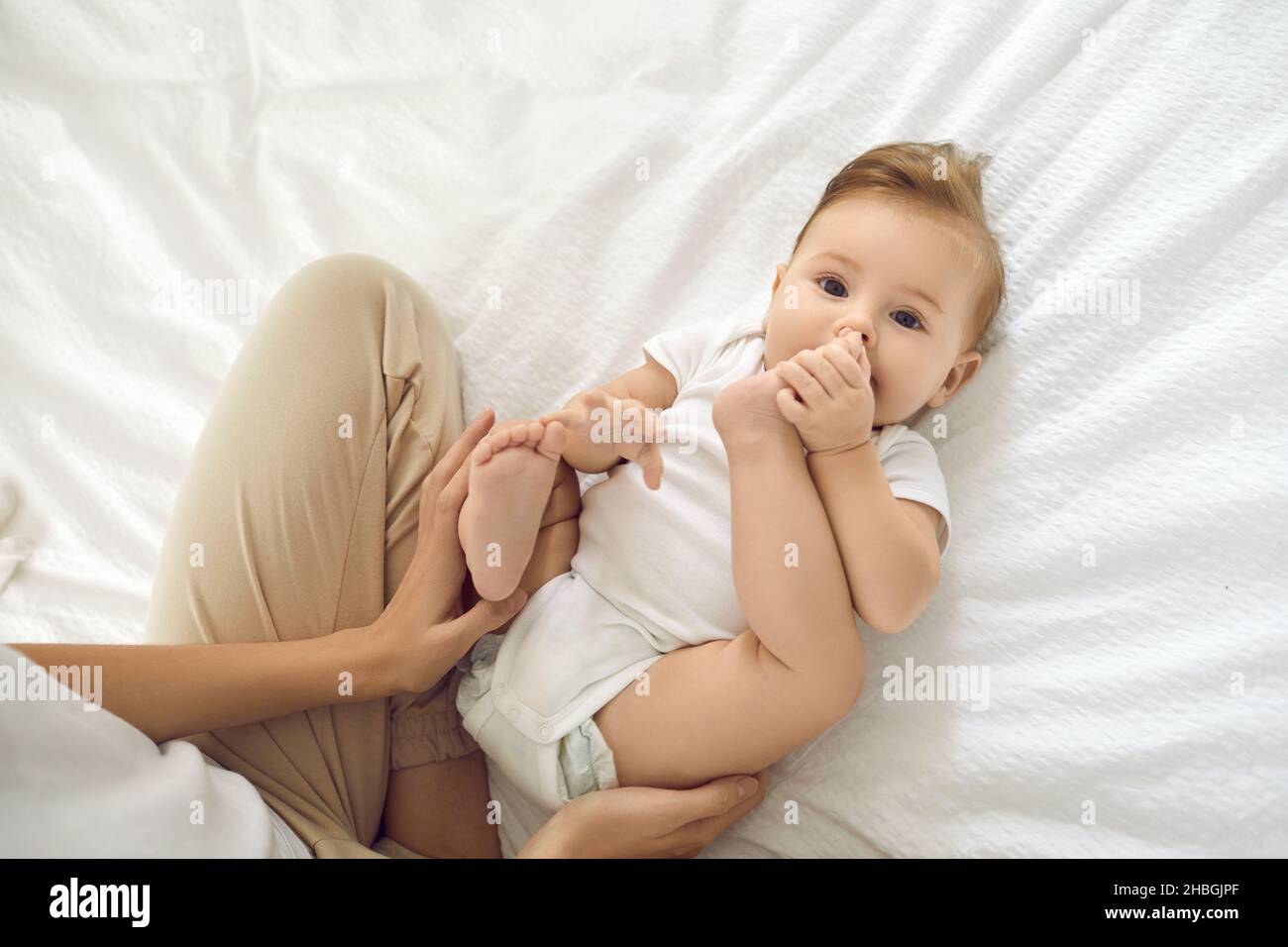 Porträt von niedlichen charmanten sechs Monate alten Mädchen spielen mit ihren Beinen auf dem Rücken auf weißem Bett liegen. Stockfoto