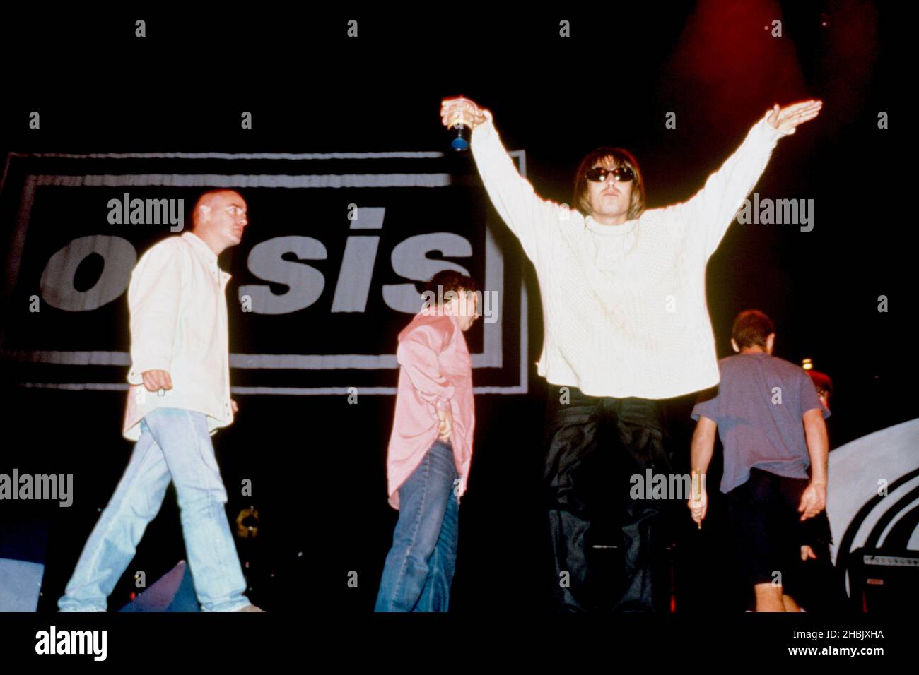 Liam Gallagher, Sänger von Oasis, krötet mit einem Pint Guinness die Menge an, während die Bandmitglieder (l-r) Bonehead (Paul Arthurs), Guigsy (Paul McGuigan), Alan White und Noel Gallagher (größtenteils versteckt) von der Bühne gehen Stockfoto