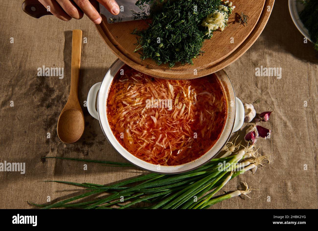 Draufsicht: Die Hände des Küchenchefs gießen gehackten frischen Dill und Knoblauch in einen Topf hausgemachter, frisch zubereiteter traditioneller ukrainischer Suppe - Borscht. Ukrai Stockfoto