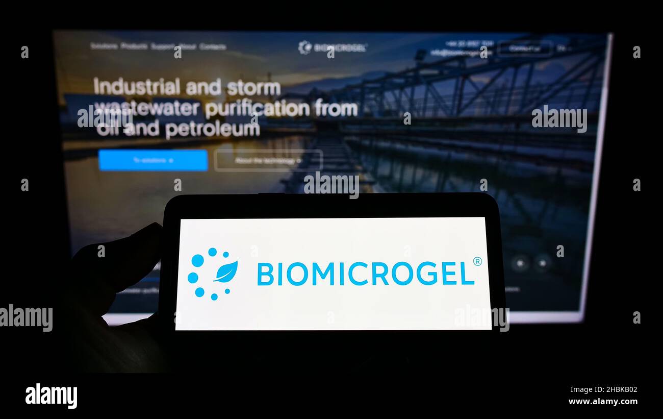 Person, die Mobiltelefon mit dem Logo der britischen Bimicrogels Group auf dem Bildschirm vor der Business-Webseite hält. Konzentrieren Sie sich auf die Telefonanzeige. Stockfoto