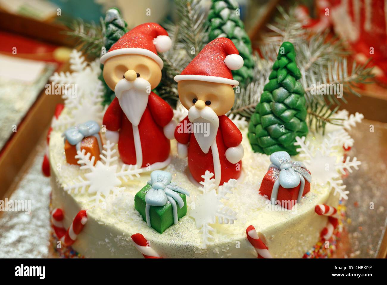 Cremiger Kuchen mit Weihnachtsmann-Figuren und süßen Weihnachtsdekorationen im Schaufenster. Konditorei, Dessert für die Neujahrfeier Stockfoto