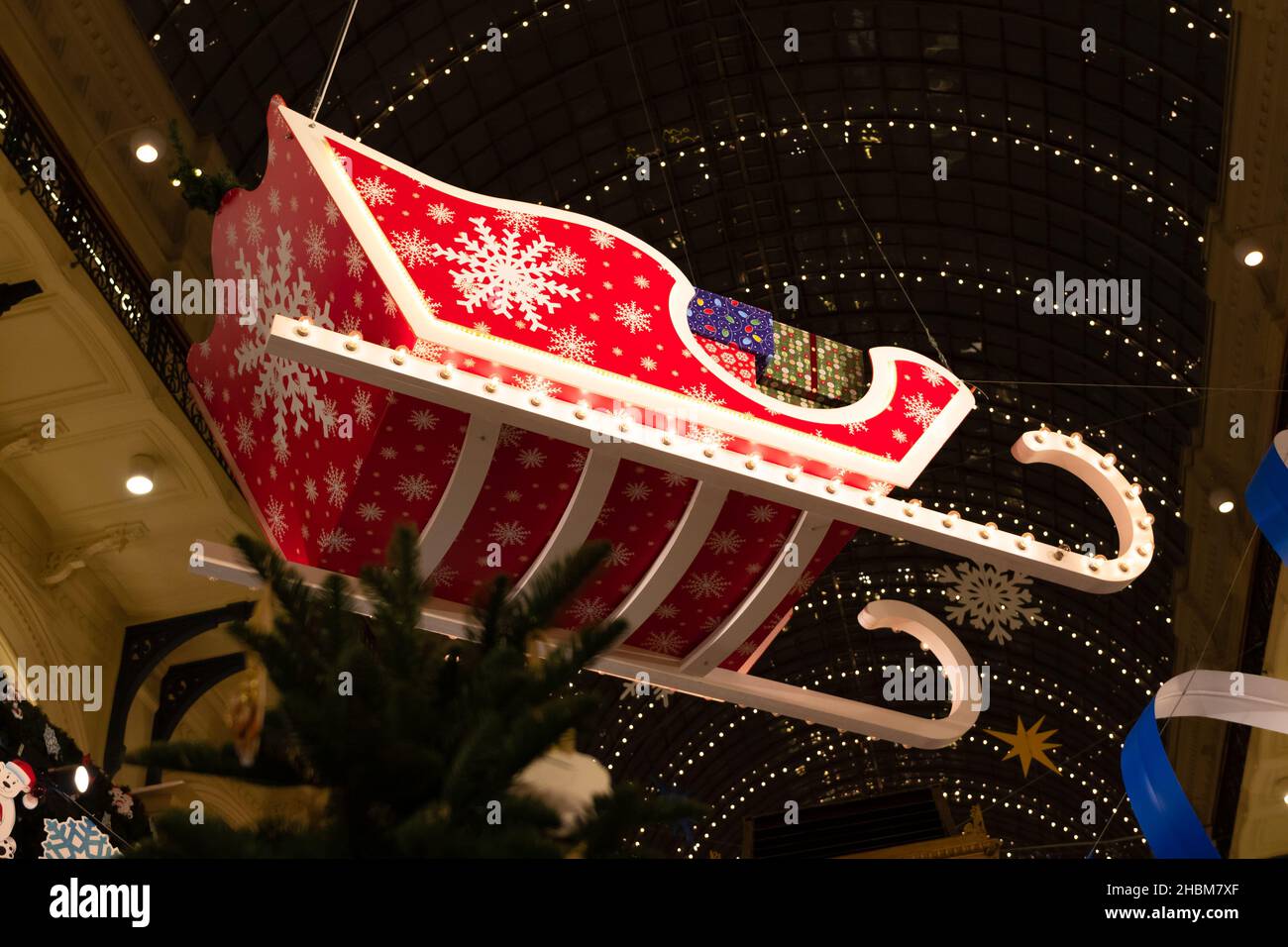Roter, heller weihnachtsmann-Schlitten mit Geschenkkartons und Schneeflocken in der Mall am Silvesterabend. Nahaufnahme Stockfoto