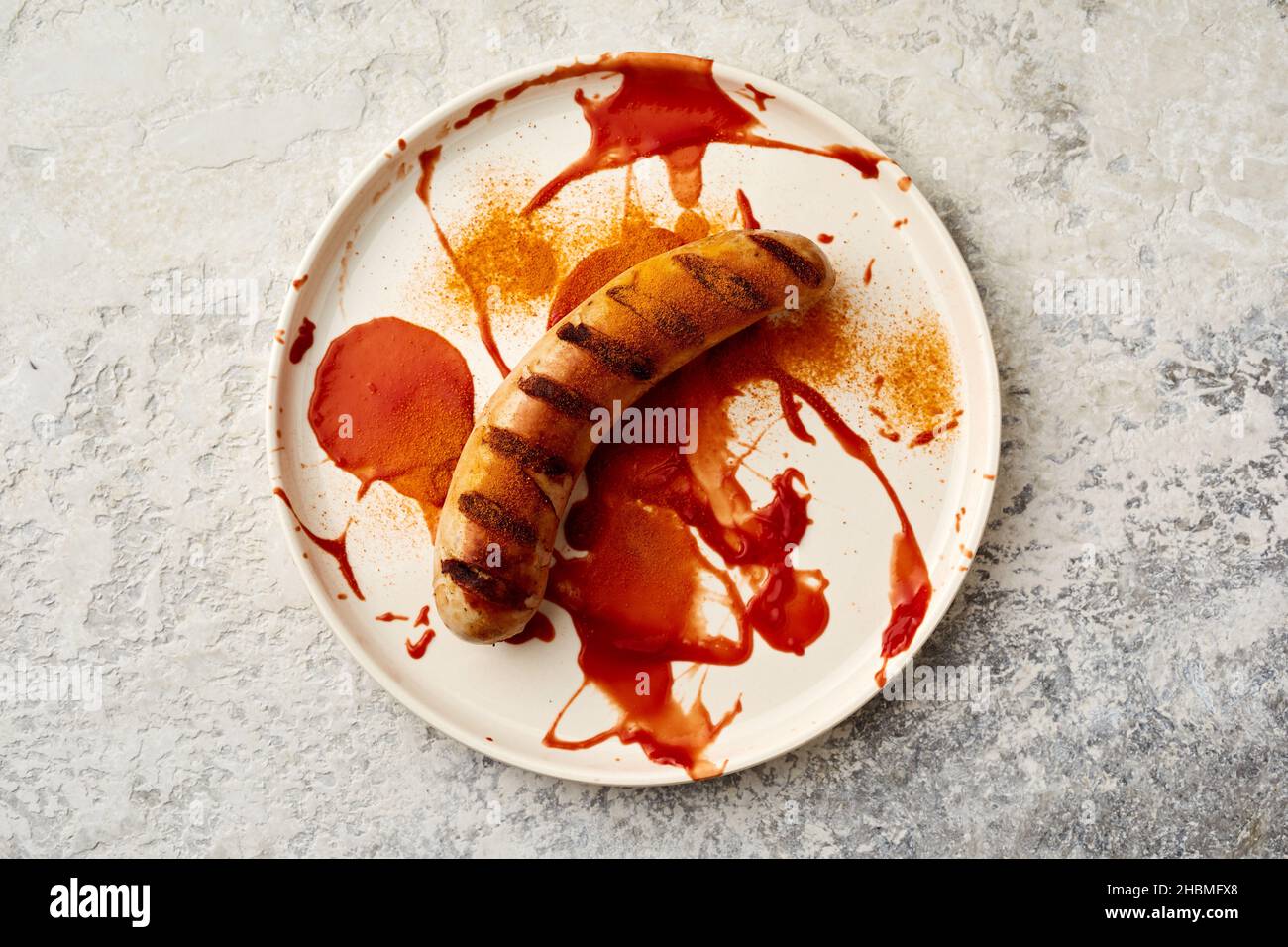 Draufsicht auf Currywurst deutsches Fast-Food-Gericht mit verschmiertem Ketchup und Curry auf Keramikplatte Stockfoto