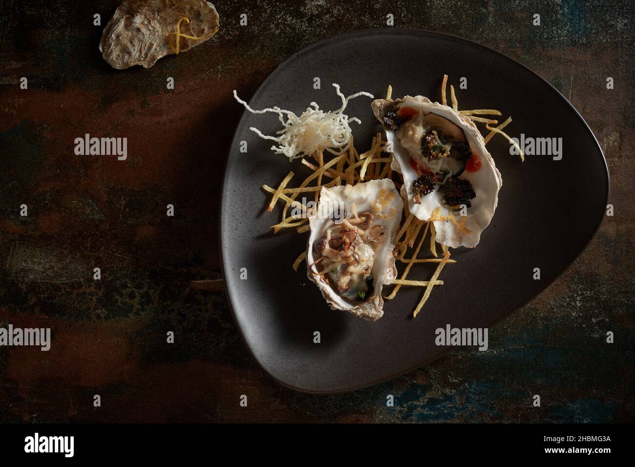 Blick von oben auf appetitlich teure, offene Austern, serviert auf schwarzem Teller auf einem schäbigen Tisch Stockfoto