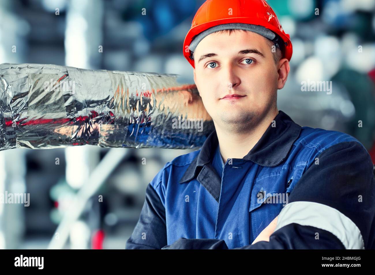 Porträt eines jungen kaukasischen Ingenieurarbeiters in Helm in den Räumlichkeiten der Fabrikwerkstatt. Industrieller Hintergrund. Stockfoto