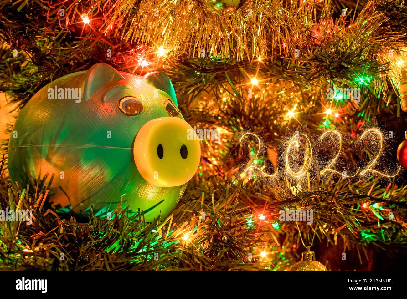 Blaues Sparschwein in einem weihnachtsbaum, mit 2022 mit Wunderkerzen geschrieben Stockfoto