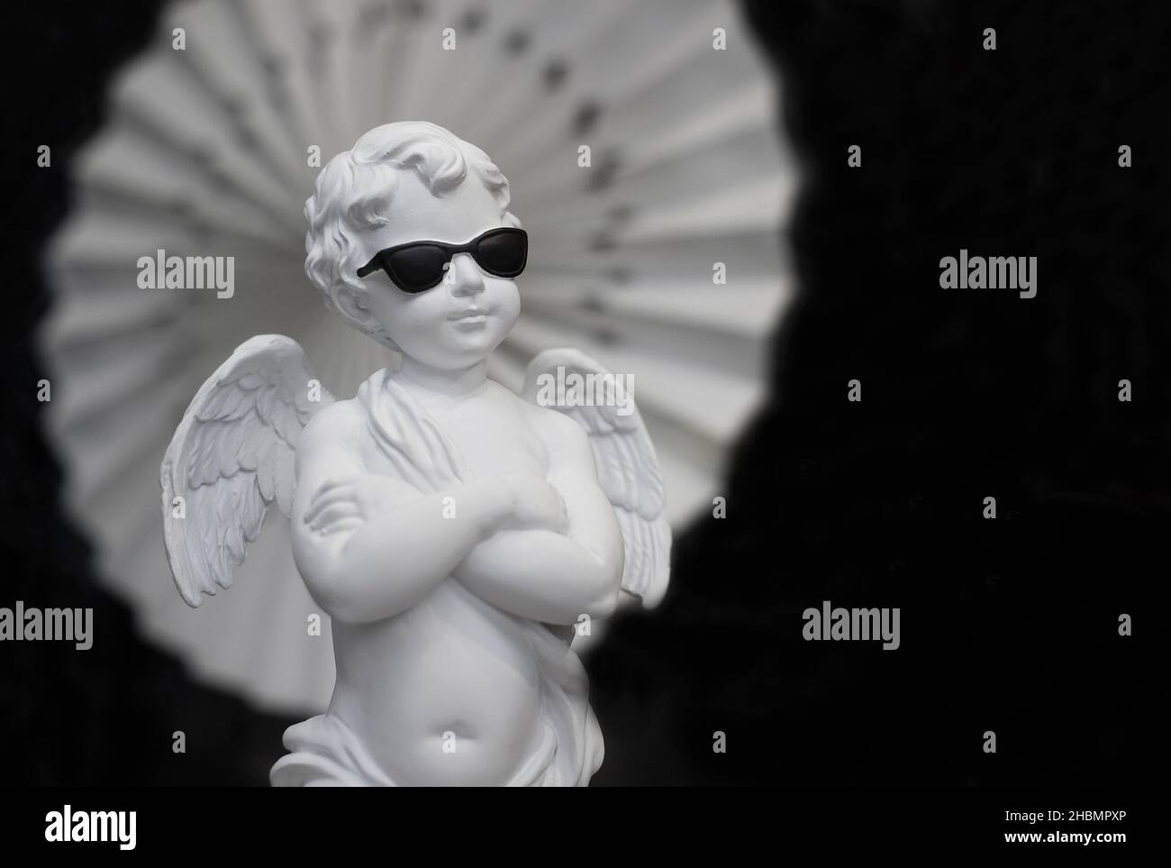 Porzellan Cherub trägt eine Sonnenbrille und die Arme sind auf schwarzem Hintergrund gefaltet Stockfoto