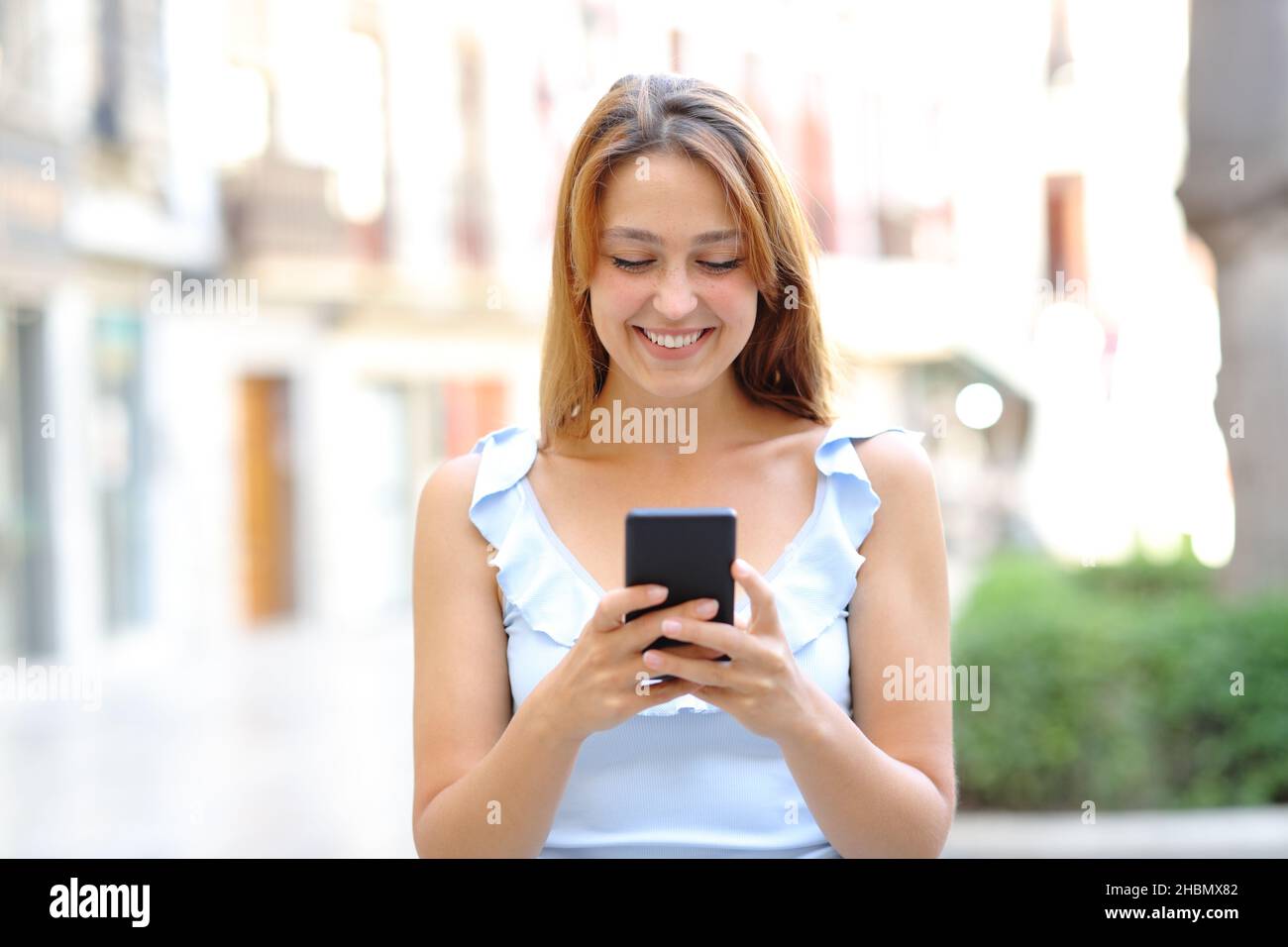Vorderansicht Porträt einer glücklichen Frau, die mit dem Smartphone auf der Straße läuft Stockfoto