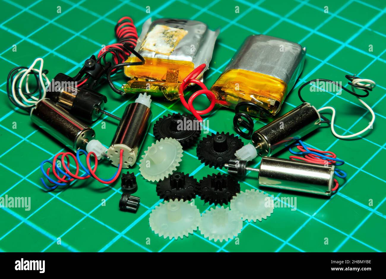 Nahaufnahme einer Gruppe von Miniatur-Elektromotoren, Nylongetrieben und Batterien auf grünem Hintergrund Stockfoto