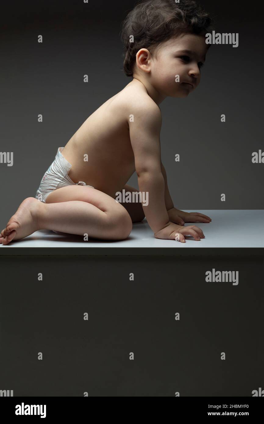 Ein einjähriges Baby mit Windel sitzt auf einer weißen Tischfläche Stockfoto