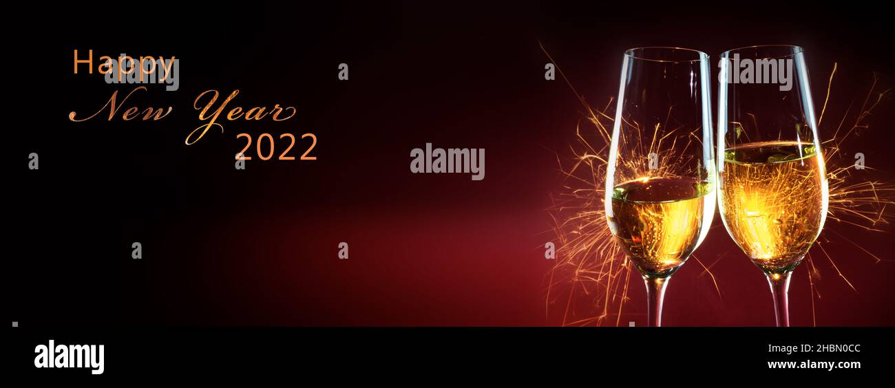 Happy New Year 2022 Text, Party Time mit zwei Sektgläsern und Feuerwerk von Wunderkerzen vor dunkelrotem Hintergrund mit Kopierfläche im Panorama Stockfoto