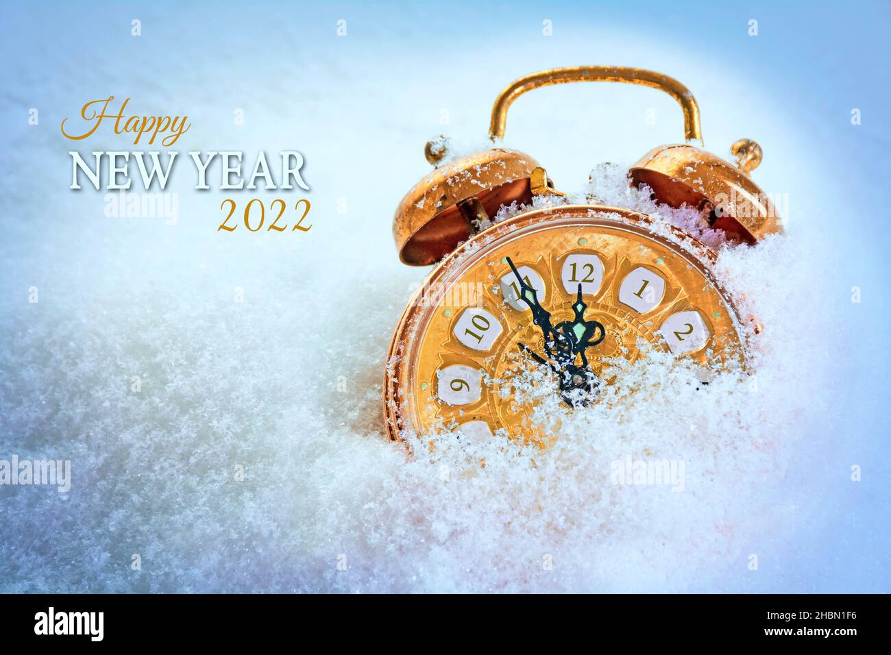 Kupferfarbener Vintage-Wecker im Schnee, der fünf Minuten vor zwölf zeigt, Text Frohes Neues Jahr 2022, saisonale Grußkarte mit Kopierfläche Stockfoto