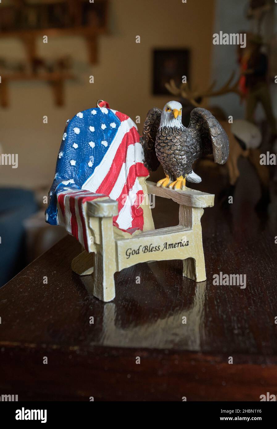 Miniaturkollektion mit einem winzigen Stuhl mit God Bless America und einer amerikanischen Flagge, die darüber drapiert ist, und einem Weißkopfadler, der auf dem Arm steht. Stockfoto