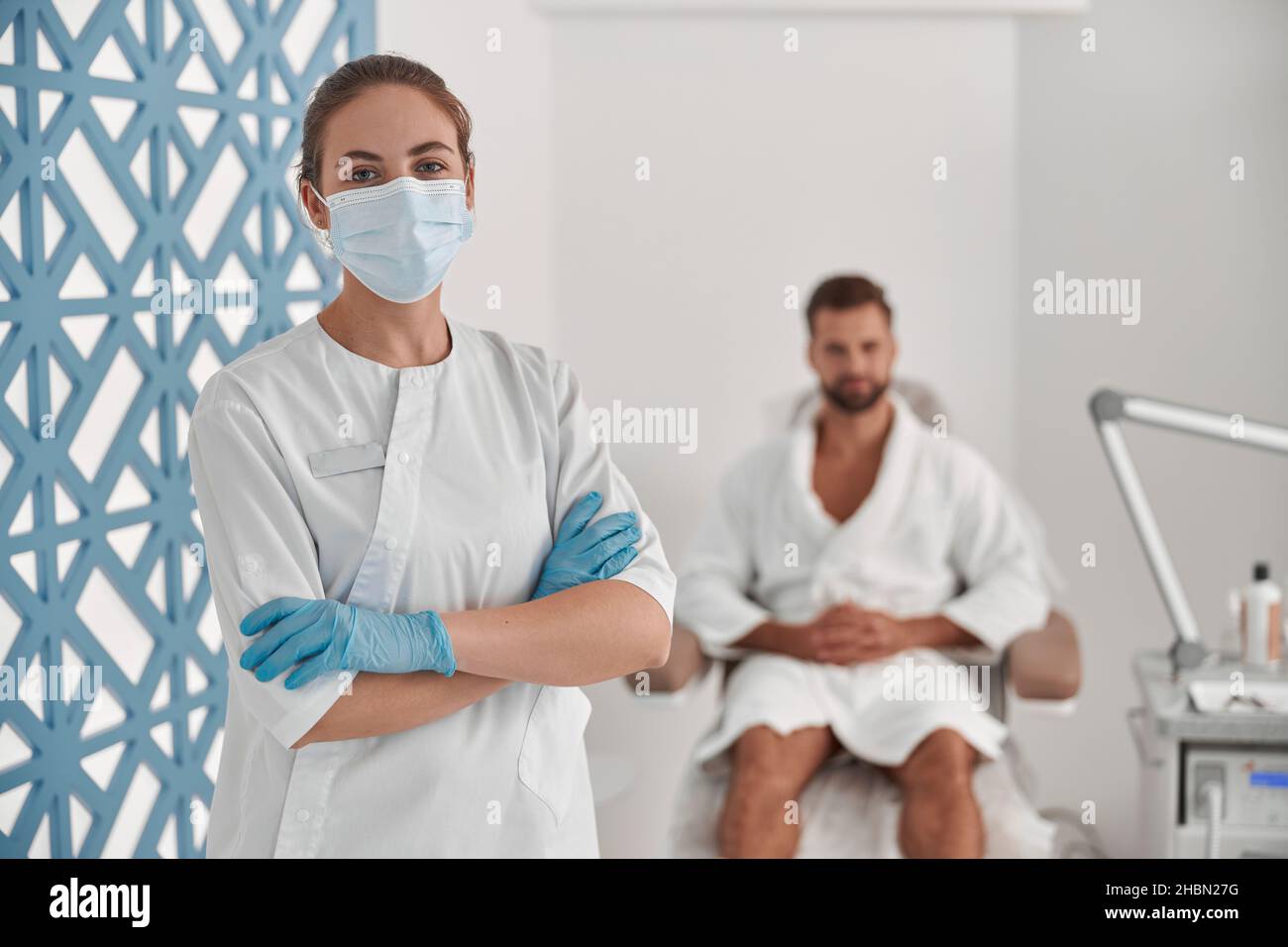 Porträt der professionellen Kosmetikerin in Schutzmaske und Handschuhe in der Nähe des Patienten in der Kosmetikklinik Stockfoto