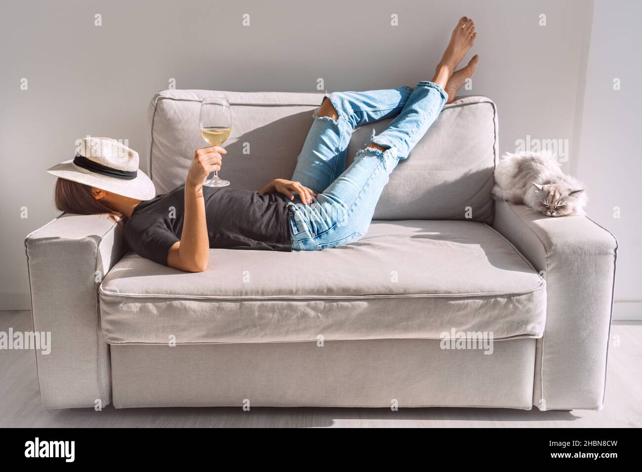 Junge Frau mit einem Glas Weißwein, der zu Hause auf dem Sofa ruht. Frau genießt Freizeit und faules Wochenende. Stockfoto