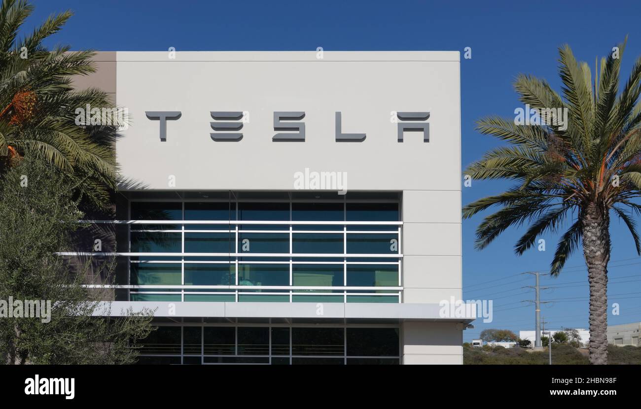 Carlsbad, CA USA - 12. Dezember 2021: Tesla-Schild auf einem kalifornischen Händlergebäude, eingerahmt von Palmen und blauem Himmel Stockfoto