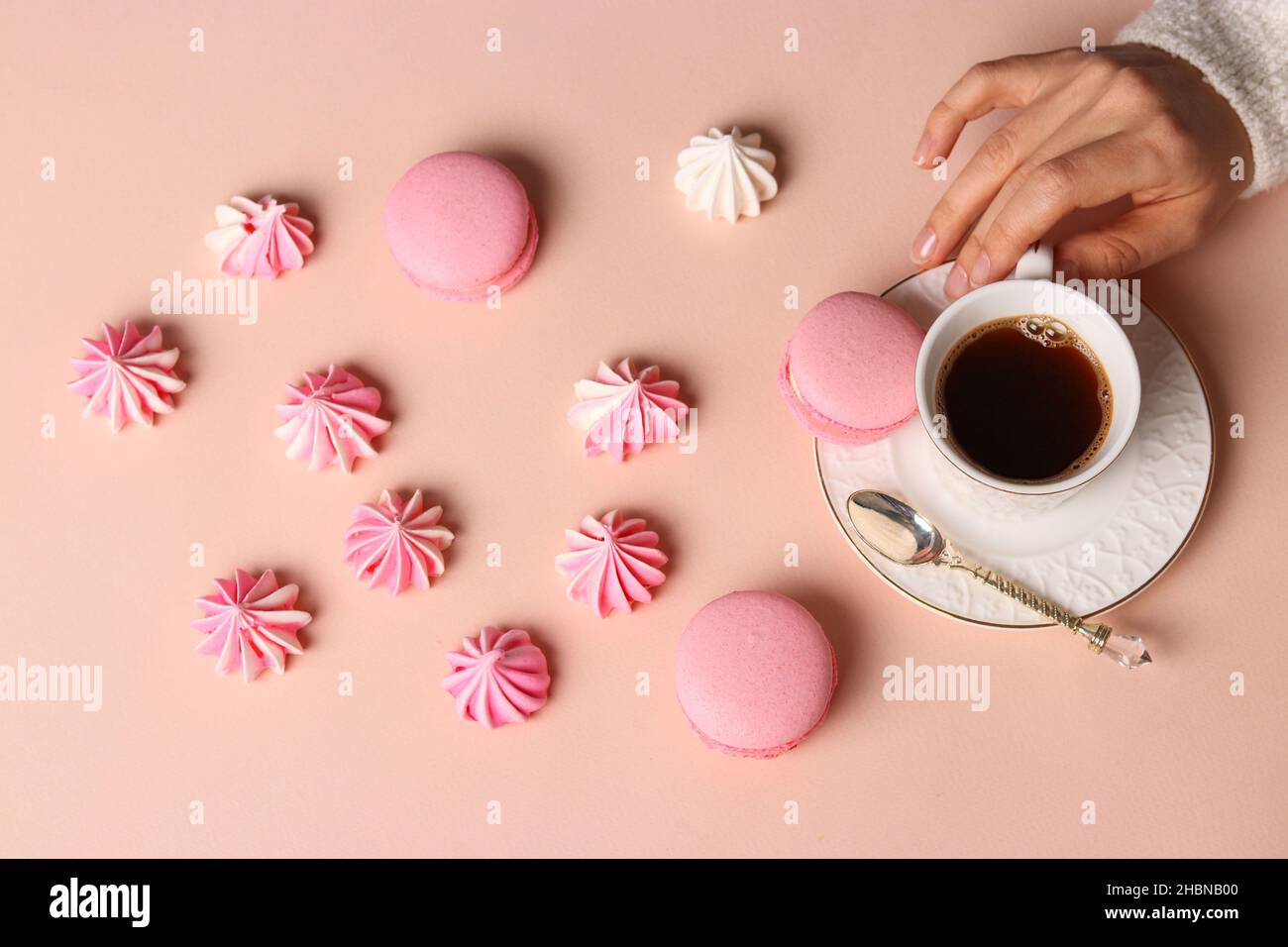 Baiser Plätzchen und Makronen auf einem rosa Hintergrund, Tasse Kaffee und Frauen Hände Stockfoto