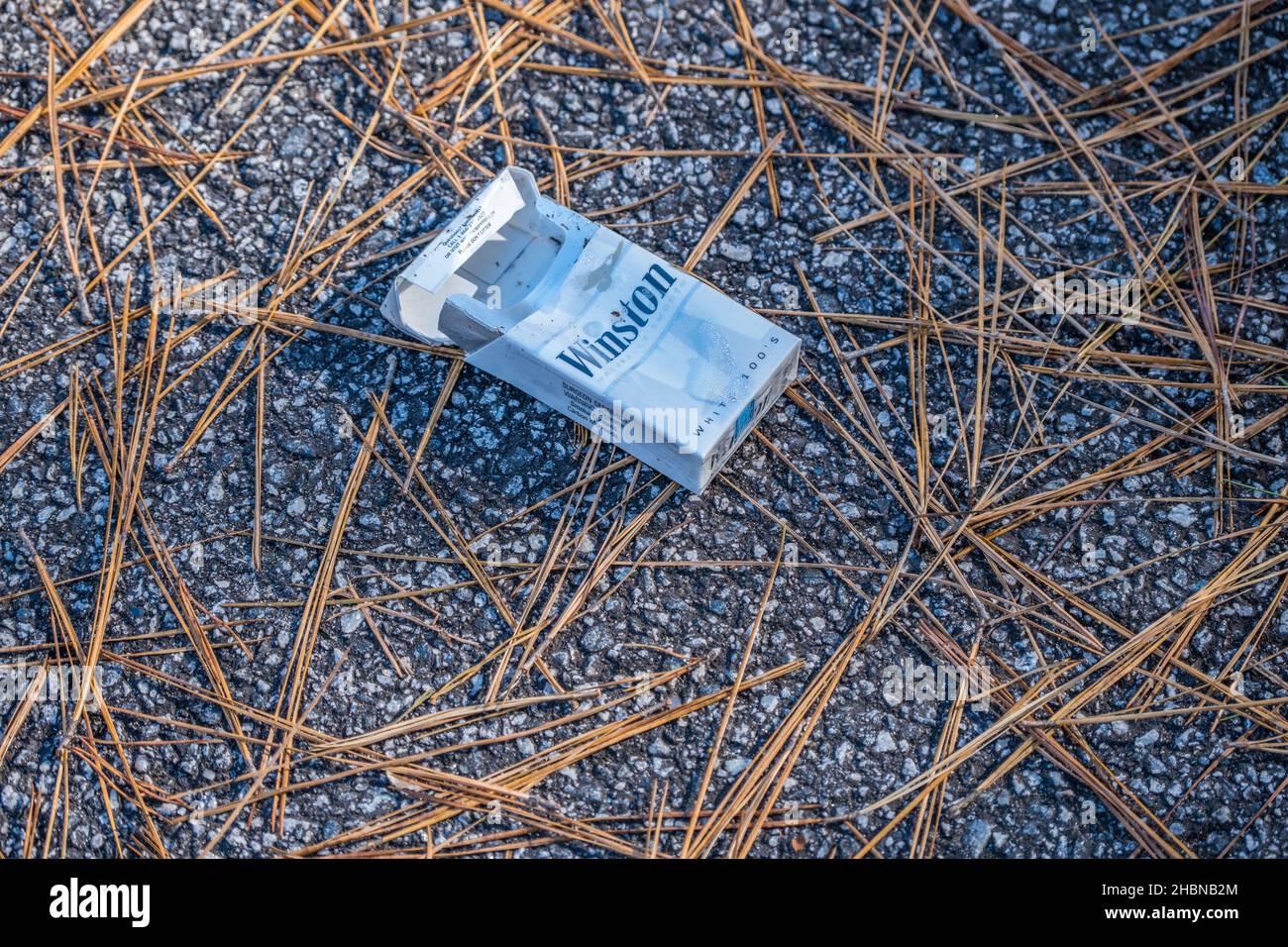 Eine ausrangierte Packung mit winston-Zigaretten hat immer noch eine geöffnete und leere Plastikfolie auf dem Parkplatzgelände im Park, die die Umwelt verschmutzt Stockfoto