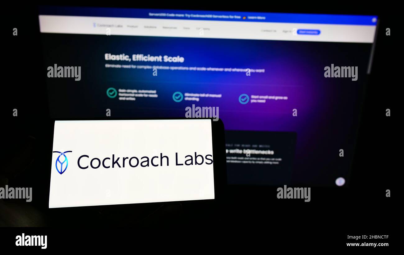 Person, die Mobiltelefon mit dem Logo des US-SQL-Datenbankunternehmens Cockroach Labs Inc. Auf dem Bildschirm vor der Business-Webseite hält. Konzentrieren Sie sich auf die Telefonanzeige. Stockfoto