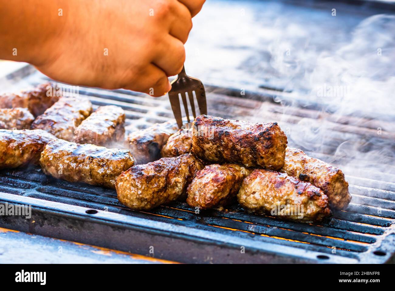 Eine Nahaufnahme der Hand eines Mannes, der auf dem Grill Fleischbrötchen zubereitet Stockfoto