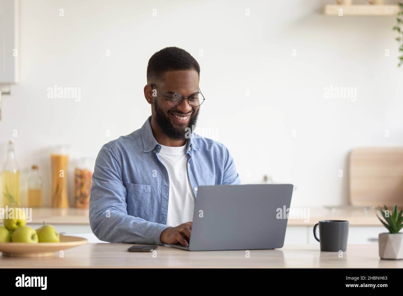 Zufriedener junger afroamerikanischer bärtiger Mann mit Brille, die am Laptop arbeitete Stockfoto