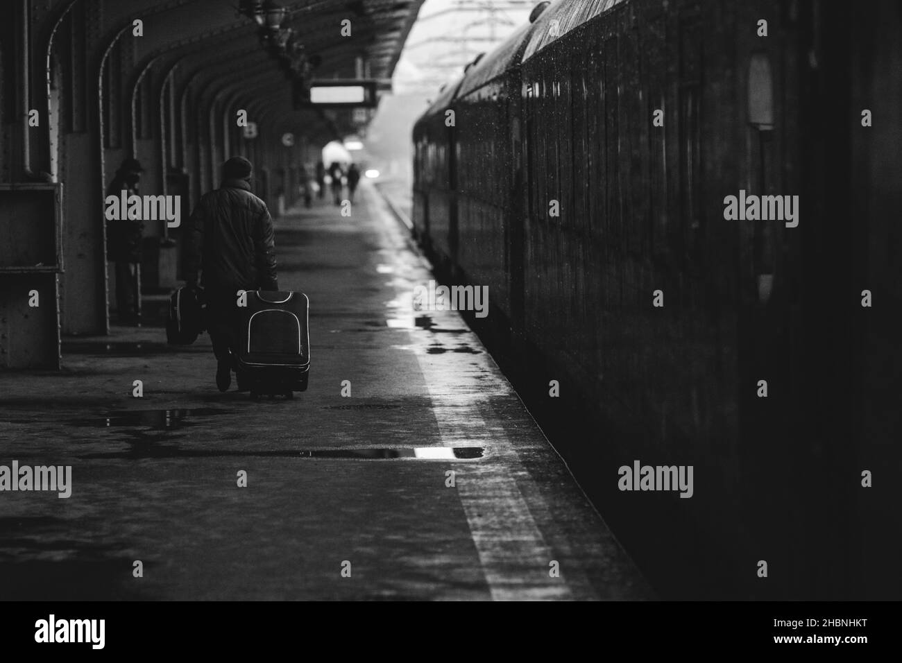 Schwarz-weiß und (Film noir, atmosphärisch) Bild mit einem Mann, der ein Gepäck in der Nähe eines Zuges trägt, bereit, von einem Bahnhof in einem verschneiten kalten Winter abzufahren Stockfoto
