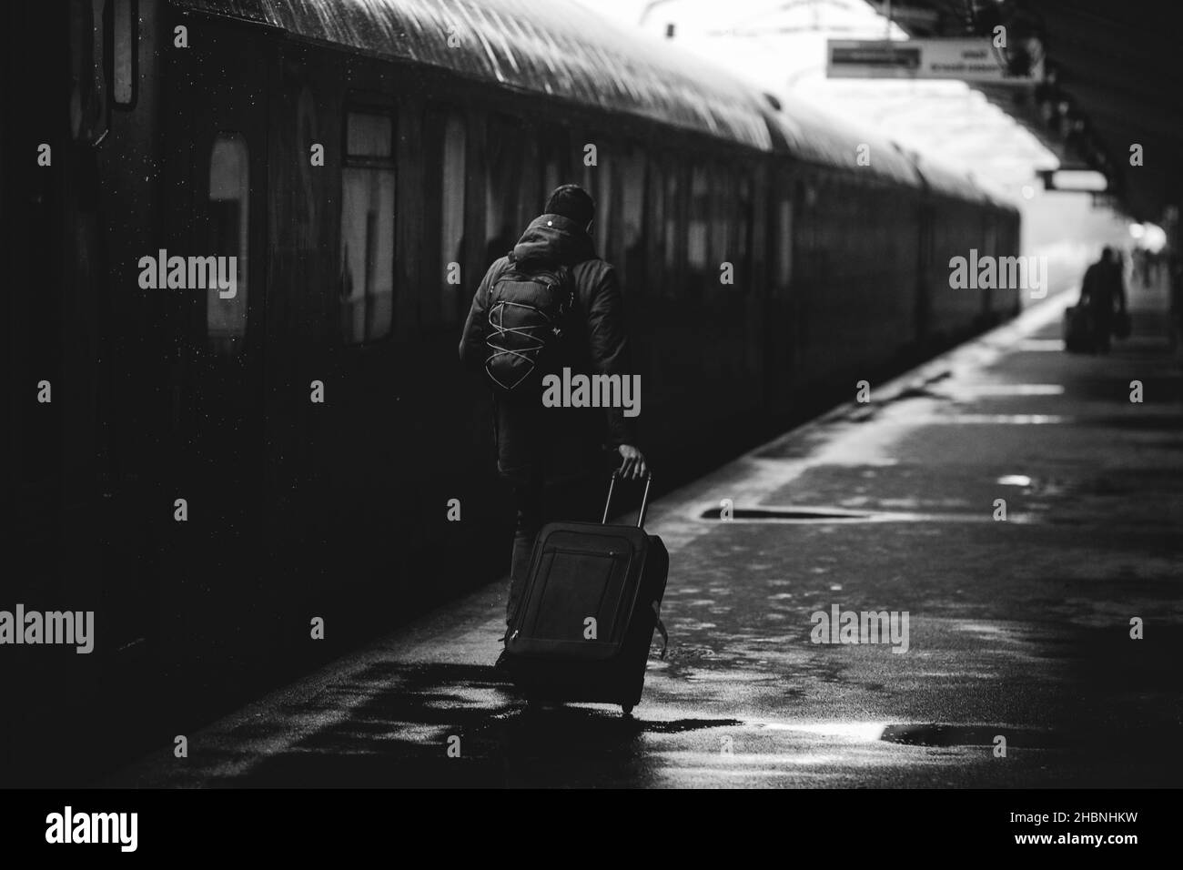 Schwarz-weiß und (Film noir, atmosphärisch) Bild mit einem Mann, der ein Gepäck in der Nähe eines Zuges trägt, bereit, von einem Bahnhof in einem verschneiten kalten Winter abzufahren Stockfoto