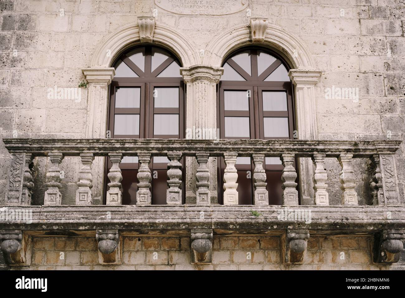 Steinbalkon mit geschnitzten Balustern und braunen Glastüren mit Pilastern Stockfoto