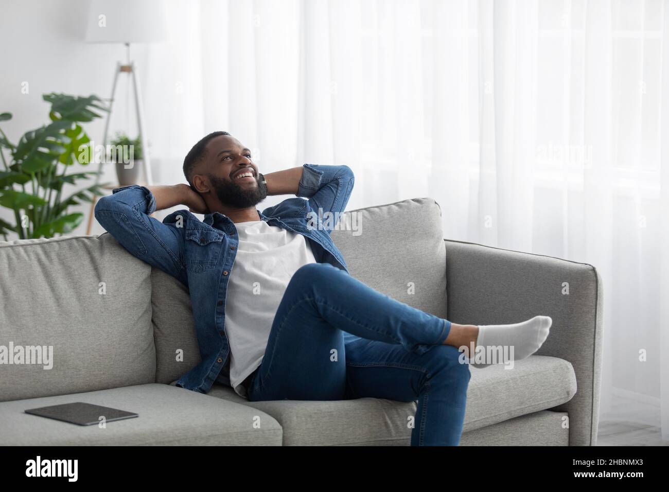 Glücklich zufrieden entspannt jungen schwarzen bärtigen Mann ruht im Wohnzimmer mit Tablet auf Sofa Stockfoto