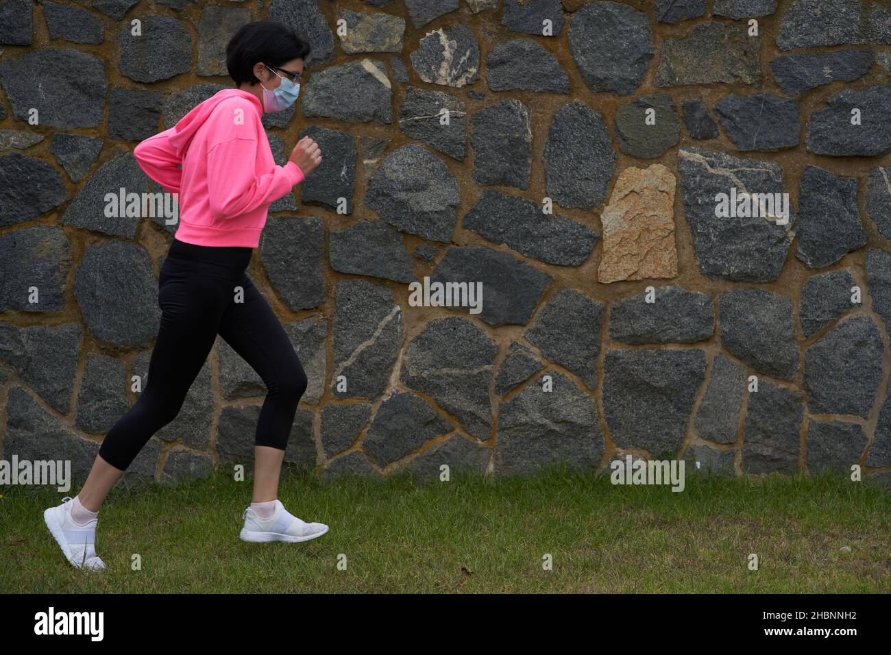 Maskierte Frau joggt im Gras. Neuer Normalwert. Sportveranstaltung Stockfoto