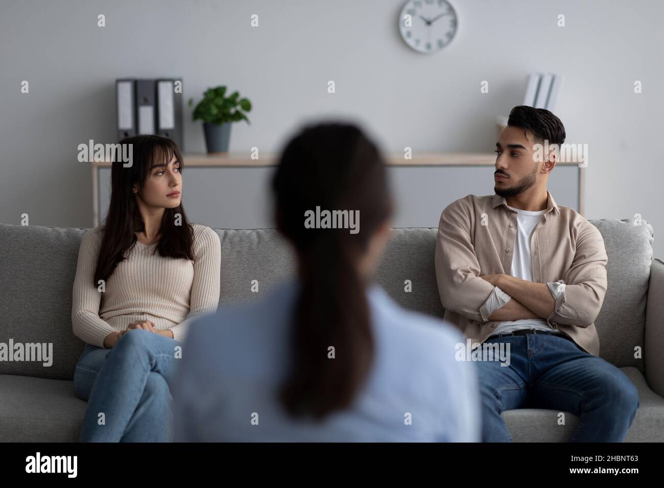 Rückansicht einer Psychologin, die ein arabisches Paar auf der Couch sitzend und sich gegenseitig angeschaut hat, mit einer Therapiesitzung behandelt Stockfoto