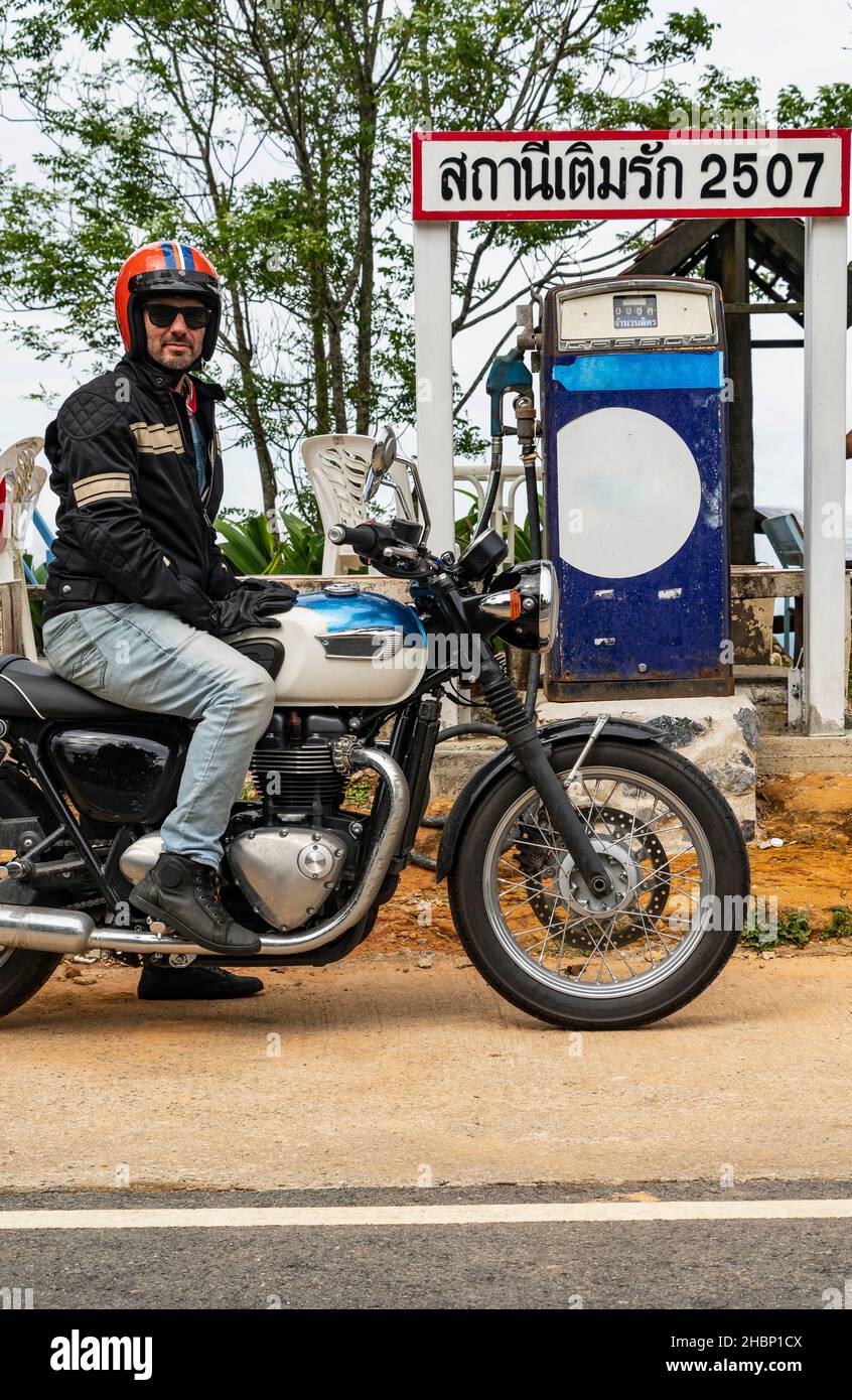Der Mann hält mit seinem klassischen Motorrad an einer alten Tankstelle Stockfoto