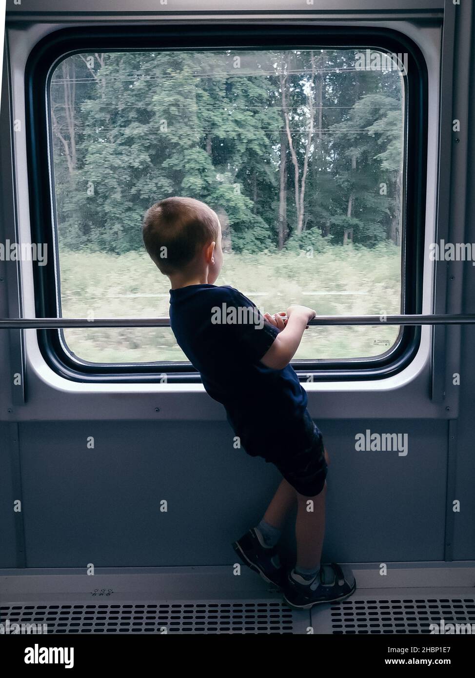 Kleiner Junge, der aus dem Fenster auf einen Reitzug schaut Stockfoto