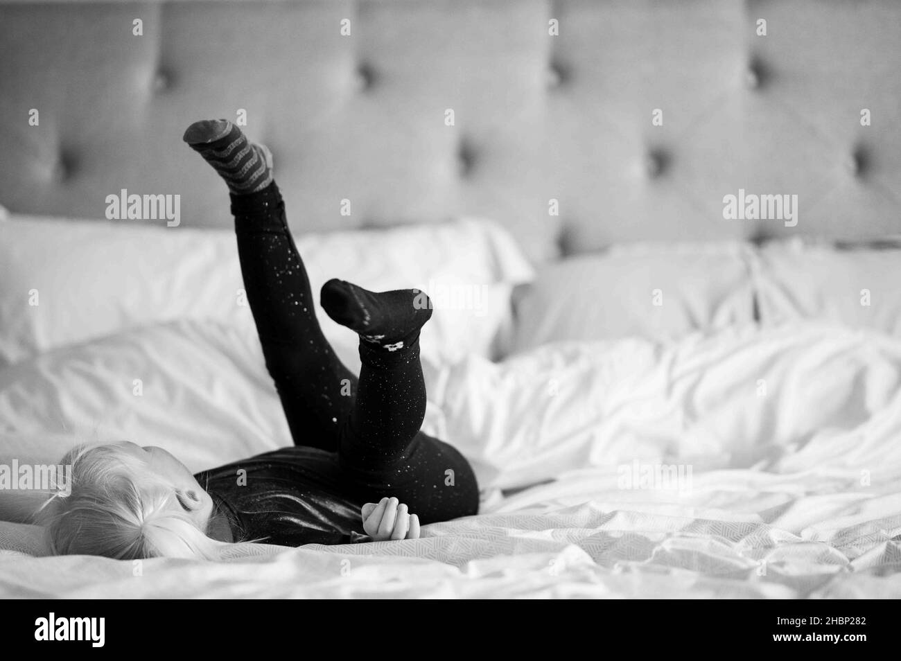 Schwarz-weißes Mädchen auf dem Bett mit Füßen in der Luft Stockfoto