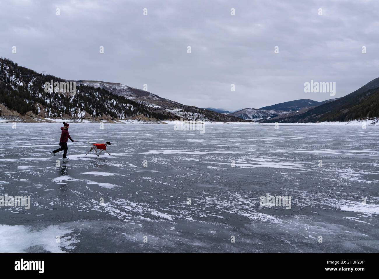 Frau Eislaufen hinter Hund auf gefrorener Landschaft während des Urlaubs Stockfoto