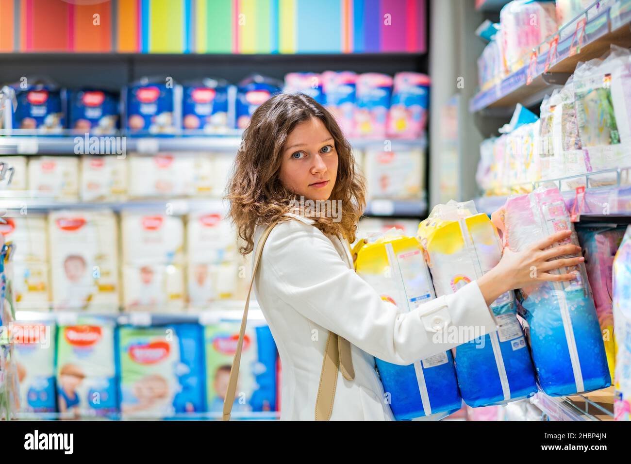 Junge Frau, Mutter im weißen Mantel, kauft Windeln für den zukünftigen Gebrauch, Mutter vieler Kinder im Supermarkt Stockfoto