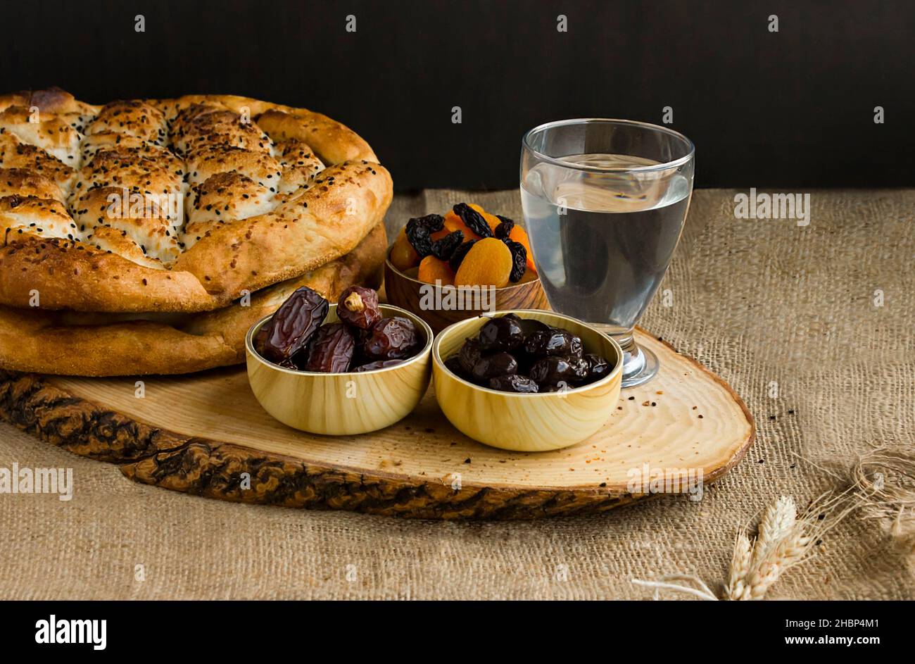 Iftar-Mahlzeit, „brechen Sie das Fasten“ mit süßen trockenen Datteln, Aprikose, schwarzen Oliven, Wasser und Ramadan-Brot auf dem Holzbrett. Beginn der Mahlzeit vor dem Hauptmenü Stockfoto