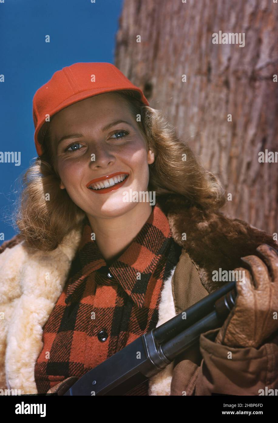 Junge Frau in Jagdkleidung und rotem Hut mit Schrotflinte Stockfoto